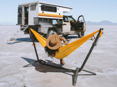 Portable Hammock Stand 15 Lb Lightweight With Quick Setup And Chair Mode Carry Bag And Straps Hang Anywhere From Home To Travel Tailgate Camping Park Or Backyard Not Included Hammock used in a desert scene with camper trailer.