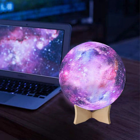 Glowing galaxy-themed orb on wooden stand beside laptop displaying similar nebula design indoors.