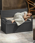 80 Gallon Outdoor Storage Bench With Wood Grain Style Resin Deck Box Waterproof And Lockable Storage Furniture in black with woman resting on it