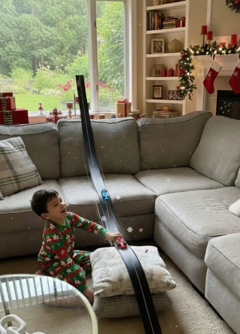 Child playing with Flexible Race Car Track Set with Pressure Suction Cups, Two Lane Slot Track, in living room during holiday season.
