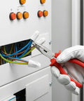 Close-up of white ceramic wire connectors being crimped onto electrical wires with red-handled pliers near a control panel.