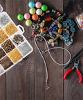 Jewelry Findings Kit With 2880 Pieces Including Open Jump Rings, Lobster Clasps, Crimp Beads, Screw Eye Pins, Head Pins, Earring Hooks And Earring Backs For DIY Jewelry Making in organized case on wooden table with beading tools and beads