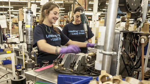 Two workers assembling washing machine valves in a factory setting.