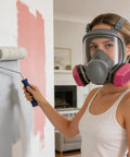 Person wearing Full Face Respirator With Filters For Sanding, Painting, Spraying And Welding, using paint roller indoors.