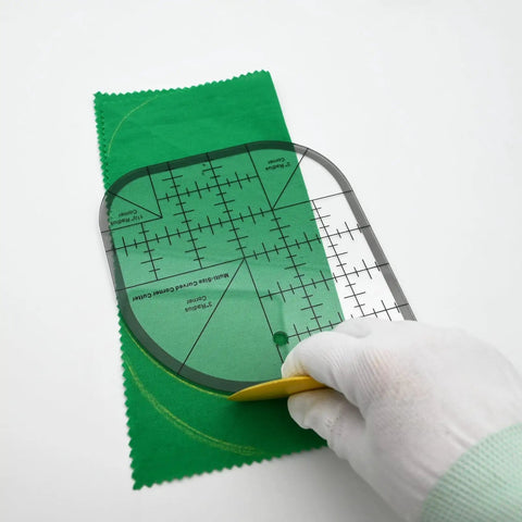 Hand using Clear Acrylic Quilting Ruler With Templates And Curved Corner Cutter For Precise Fabric Cutting on green fabric
