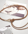 Women Knotted Skinny PU Leather Waist Belt With Gold Alloy Buckle Adjustable Double Rope Design displayed on a gray surface with fashion magazines.