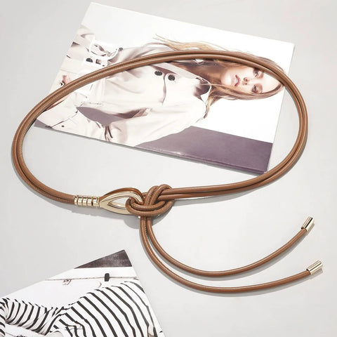 Women Knotted Skinny PU Leather Waist Belt With Gold Alloy Buckle Adjustable Double Rope Design displayed on a gray surface with fashion magazines.
