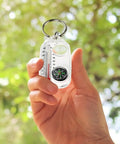 Hand holding rugged portable compass keychain, multifunction tool with thermometer, outdoors go-to direction gear, ABS construction.