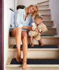 Woman and child sitting on steps with 15 Piece Indoor Stair Treads For Wooden Steps Grippy Non Slip Carpet Treads With Gray Stripe Design.