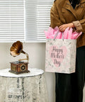 Large 13 Inch Gift Bag With Tissue Paper And Greeting Card For Mother's Day Birthdays Weddings Eco Friendly 3 Sheets Pink Tissue Included Ready To Gift In Style in woman's hand next to table.