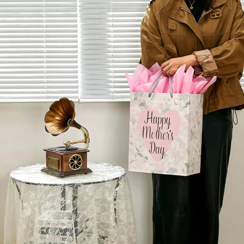 Large 13 Inch Gift Bag With Tissue Paper And Greeting Card For Mother's Day Birthdays Weddings Eco Friendly 3 Sheets Pink Tissue Included Ready To Gift In Style in woman's hand next to table.