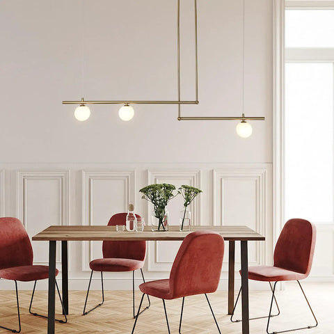 Three Light Glass Globe Linear Chandelier In Gold Finish Pendant Light above dining table with red chairs in modern room