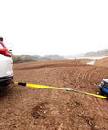 4 Pack Heavy Duty Car Trailer Tie Down Straps set in use towing car across muddy terrain, showcasing 10,000 pound break strength.