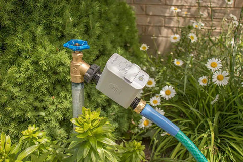 Smart Hose Watering Timer with auto scheduling attached to garden hose for precise timed watering amidst plants and flowers