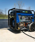 Portable blue emergency generator on wheels with handle, cable plugged in, situated on outdoor pavement, clear sky backdrop.