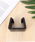 Close-up of black clip, part of Four Pack Sturdy Chair Clips For Rattan Furniture, Sofa Fasteners And Corner Connectors, on wood surface.