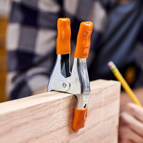 Close-up of 2 Inch Spring Clamp With Handle One Handed Clamping Tool Silver Orange Finish Quick Release Paddle Action gripping wood.