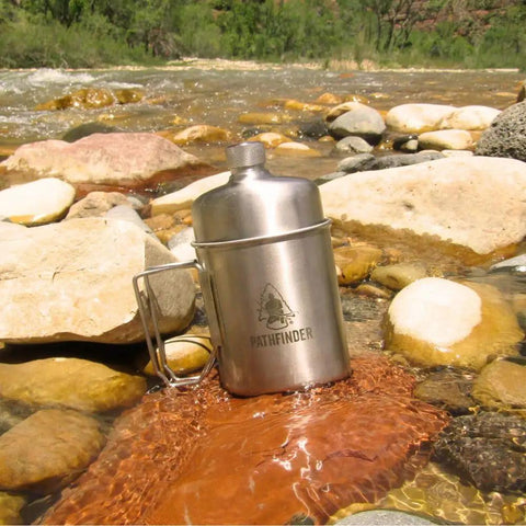 Stainless Steel Nesting Cup And M34 Scout Canteen Set For Camping And Hiking resting on river rocks