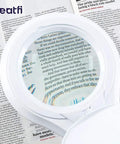 LED Magnifying Lamp With Clamp, 1,200 Lumens, 5-Inch Glass Lens, close-up view magnifying text on a page