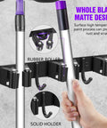 Close-up of black matte wall mount with five racks and four hooks holding brooms, mop and broom organizer wall mount with five racks and four hooks, self adhesive black garage storage, space saver for tight laundry areas, nine storage positions in one easy install.