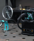 Magnetic MIG welding torch holder with turquoise base on a metal workbench; holds MIG torch.