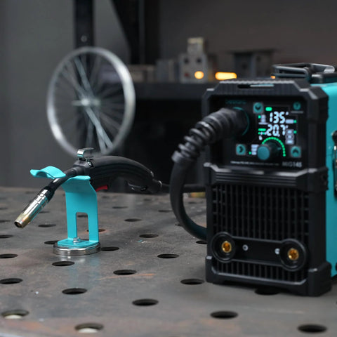 Magnetic MIG welding torch holder with turquoise base on a metal workbench; holds MIG torch.