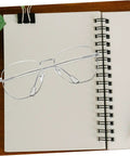 Clear glasses frame resting on a spiral notebook, representing Sunglasses Repair Kit Quick Fix For Eyeglass Temples And Replacement Arms Spare Glasses Legs Durable DIY Repair Tools For A Secure Fit And Sleek Look.