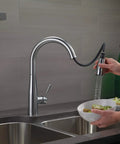 Essa Brushed Nickel Kitchen Faucet With Pull-Down Sprayer in use, rinsing a bowl of fruit, placed over double sink.