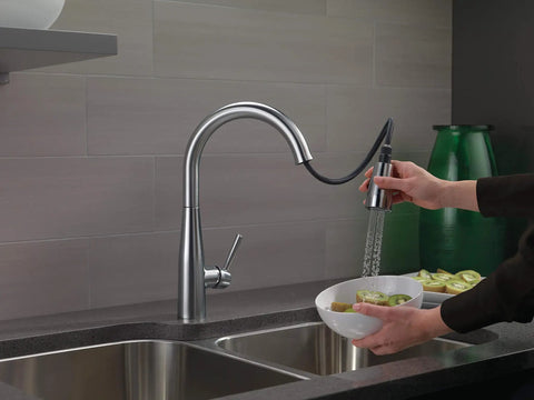 Essa Brushed Nickel Kitchen Faucet With Pull-Down Sprayer in use, rinsing a bowl of fruit, placed over double sink.