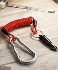 Stainless Steel RV Breakaway Cable With Transparent Jacket High Strength Lanyard, red coiled cable, metal clip, on wooden surface.