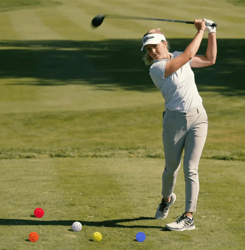 Golfer swinging club near colorful Six Pack Replacement Backyard Golf Balls With Carry Bag For Bucket Game on green field.