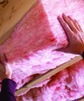Hands installing Premium Pink Fiberglass Insulation Batts For Interior Walls And Attic Cavities, showcasing its soft unfaced design.