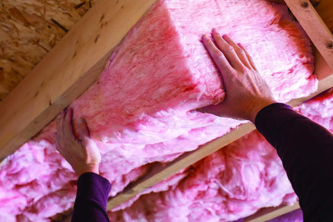 Hands installing Premium Pink Fiberglass Insulation Batts For Interior Walls And Attic Cavities, showcasing its soft unfaced design.