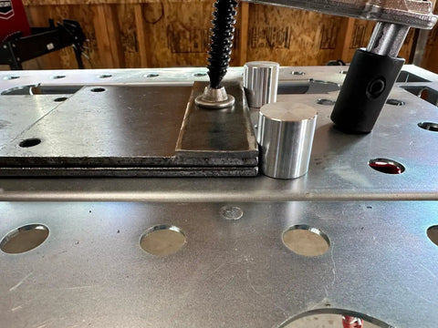 Close-up of welding table with two aluminum alignment pins from the Welding Table Fixture Pins Kit For Shop Fixturing 12 Pieces Five Eighths Inch By One Inch By One Point Five Inch Aluminum Alignment Pins For Square And Round Tubes V Groove Stops Quick Setup Fixturing