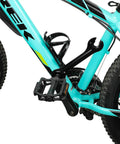 Close-up of a mountain bike pedal and chain area with turquoise frame, featuring rugged tires and black pedal detail.
