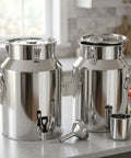 Two stainless steel milk cans with airtight lids, spigot, and funnel in a kitchen. Stainless Steel Milk Can With Airtight Lid Built To Last Heavy Duty Food Grade Tank For Milk Storage And Easy Transport In A Commercial Kitchen Water Dispenser Style Pail Buckets For Home Cafe Use