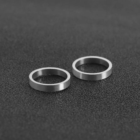 Two silver aluminum alloy bicycle chainring bolt spacers washers lying flat on black surface, 2mm thick, 10mm inner diameter.