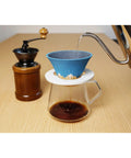 Pouring water into a blue coffee dripper on a glass carafe, featuring a solid yellow ceramic coffee filter reusable pour over dripper kit.