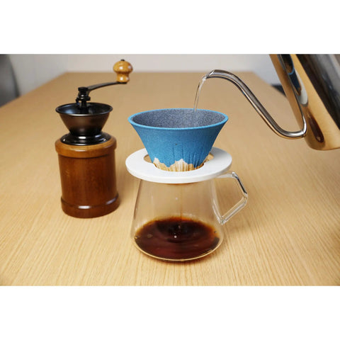 Pouring water into a blue coffee dripper on a glass carafe, featuring a solid yellow ceramic coffee filter reusable pour over dripper kit.