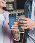 Hands holding blue and gray 16 Oz Disposable Paper Coffee Cups With Lids, Sleeves, And Stir Sticks, Blue And Gray, 100 Pack.