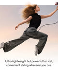 Person in motion holding Supersonic Travel Hair Dryer With Universal Voltage For On The Go Styling Ultra Lightweight And Compact Design.