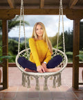 Woman sitting on Boho Macrame Swing Chair For Indoor And Outdoor Use, Durable Cotton Hanging Hammock with tassels, patio view.