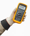 Person holding Pro Grade True RMS Digital Multimeter Kit With Premium Leads, displaying screen and controls, rugged design visible.