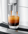 Close-up of automatic espresso machine with 17 coffee specialties, brewing espresso into glass, premium piano white finish.