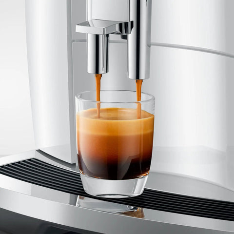 Close-up of automatic espresso machine with 17 coffee specialties, brewing espresso into glass, premium piano white finish.