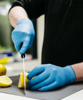 Blue nitrile disposable gloves worn by a person slicing a lemon on a cutting board.