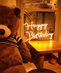 Happy Birthday LED Neon Sign 18 Inch For Backdrops And Parties, Warm White Neon Light Decor next to teddy bear on table