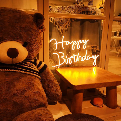 Happy Birthday LED Neon Sign 18 Inch For Backdrops And Parties, Warm White Neon Light Decor next to teddy bear on table