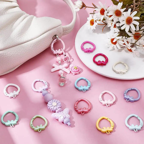 14 Color Spring Gate Ring Set For Keychains And Craft Projects With Strawberry Trigger Snap Buckles displayed on pink surface with flowers and bag
