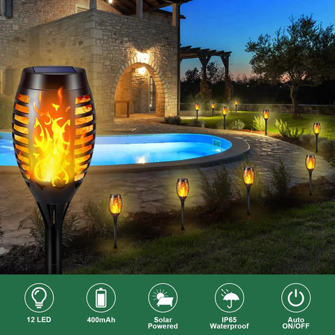 8 Pack 12 LED Solar Torch Lights With Flickering Flame illuminating a garden pathway near a pool at night, outdoor decor.